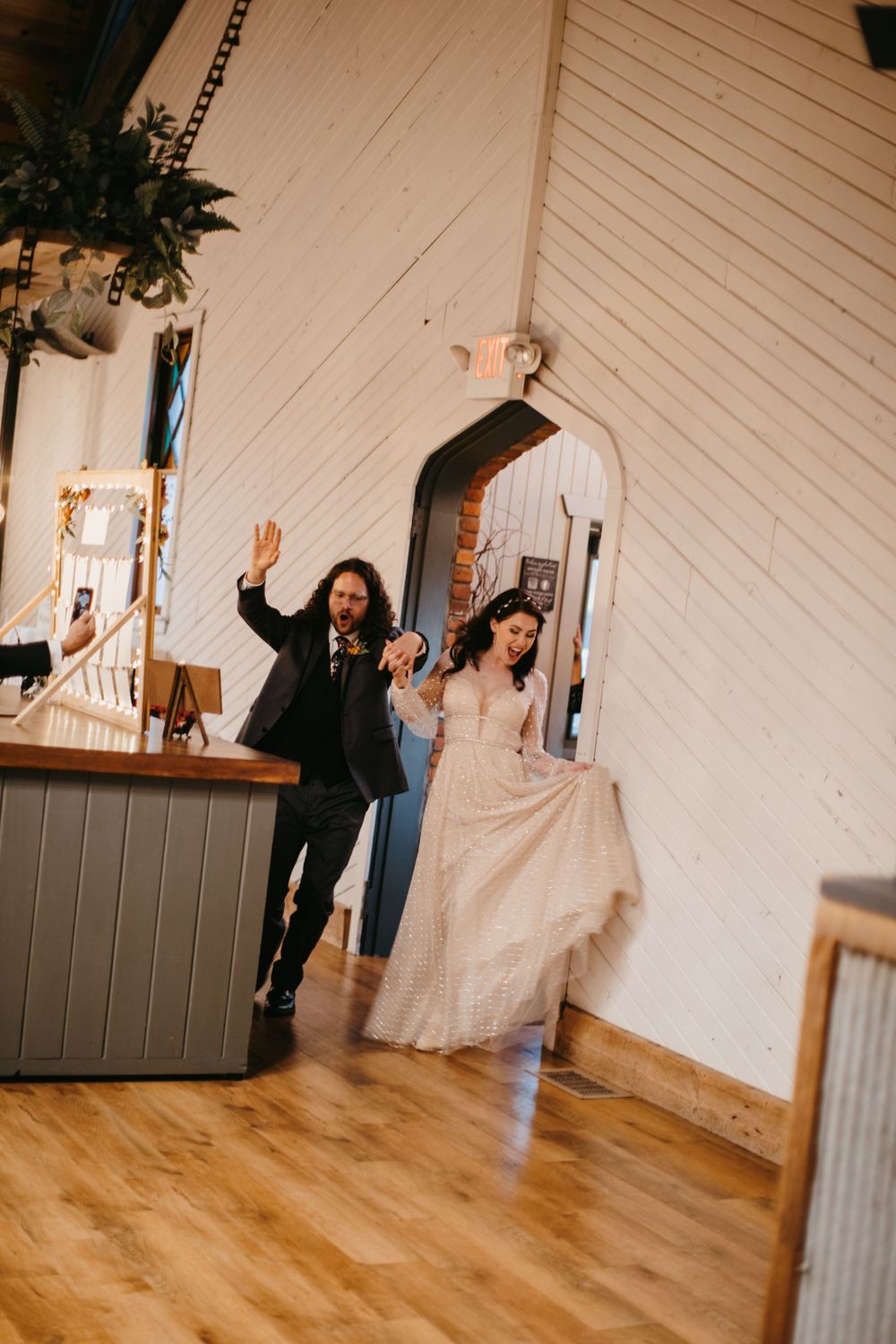 Excited bride and groom enter their rustic white barn wedding reception waving to their guests.