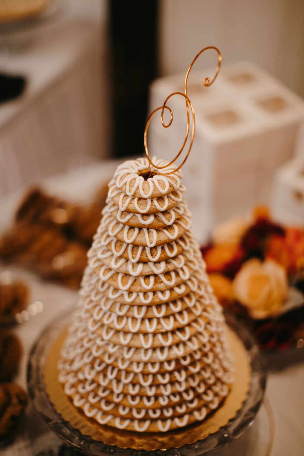 Elegant kransekake Norwegian wedding cake tower topped with a gold decorative monogram on a glass cake stand.