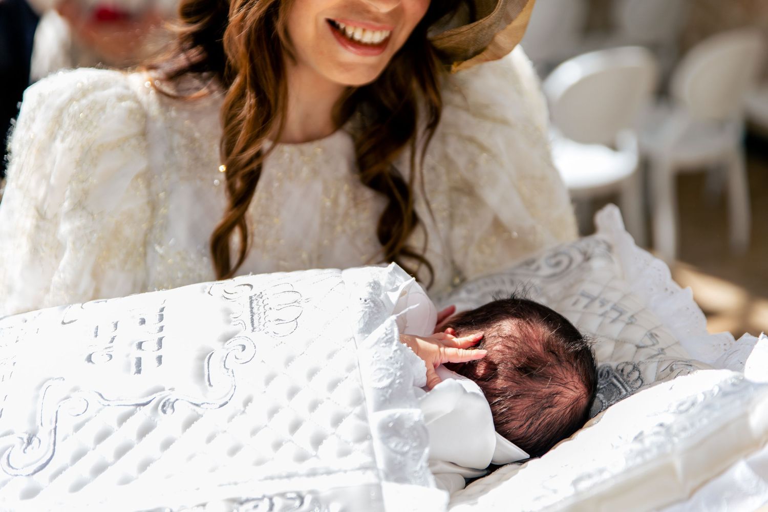 A joyful new mother in a white dress holding and looking down at her newborn baby.