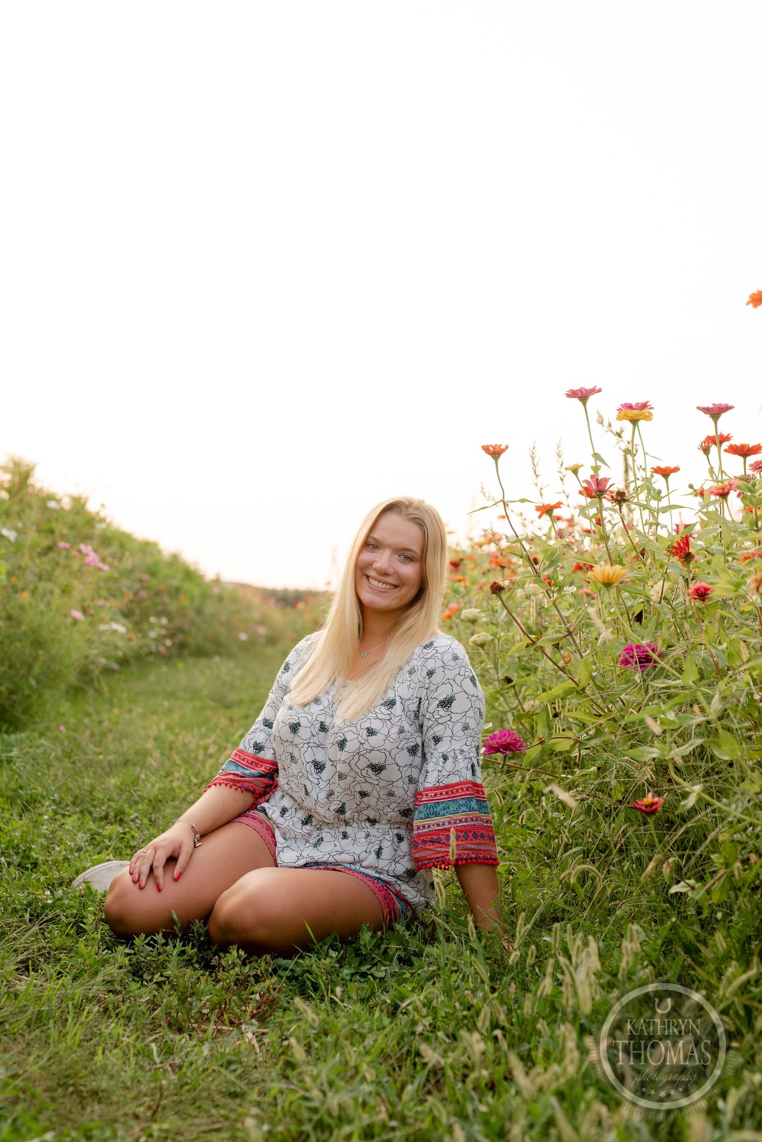 Sitting peacefully in a floral dress among blooming wildflowers at sunset.