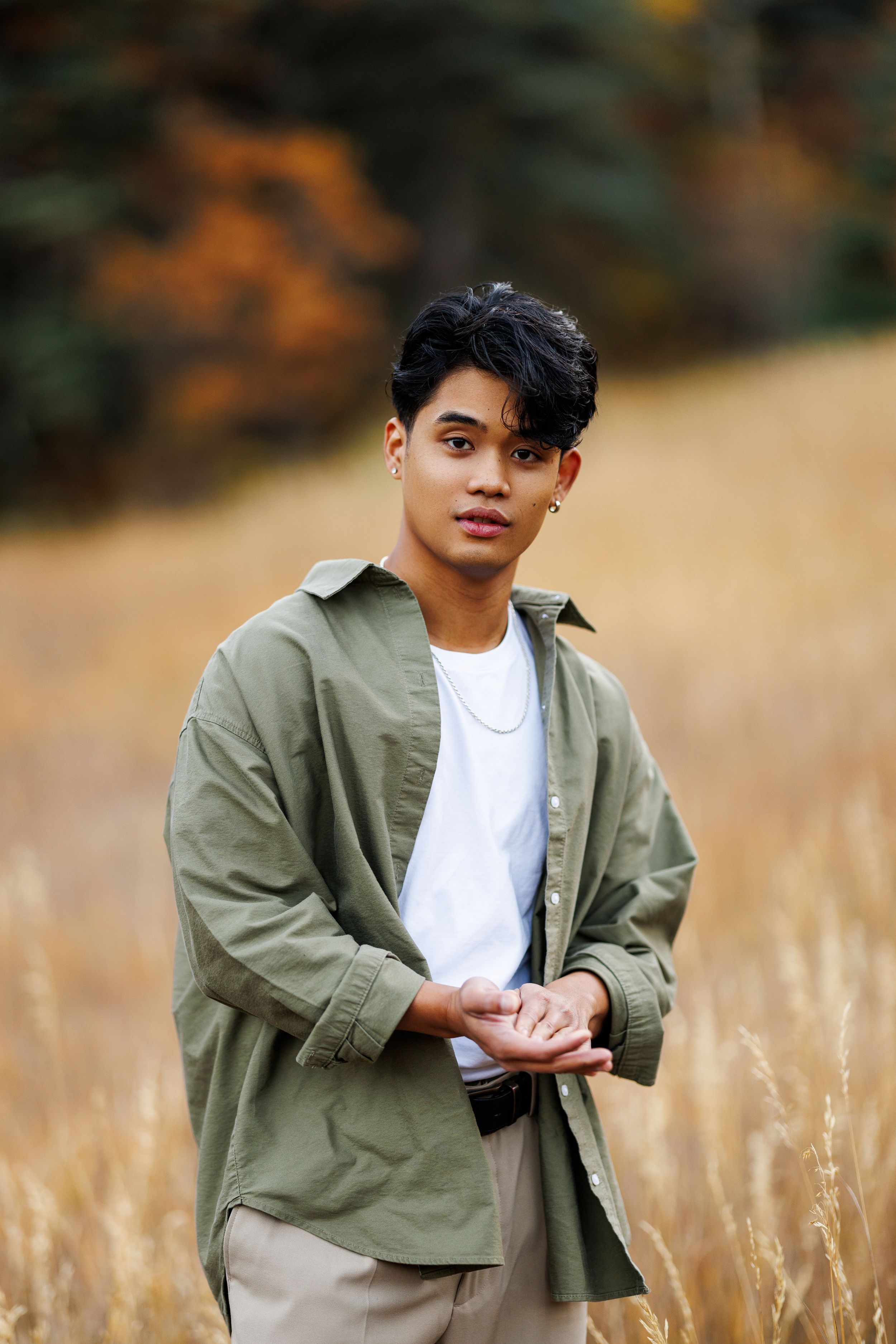 Portrait of someone in an olive jacket and white shirt standing in a golden wheat field.