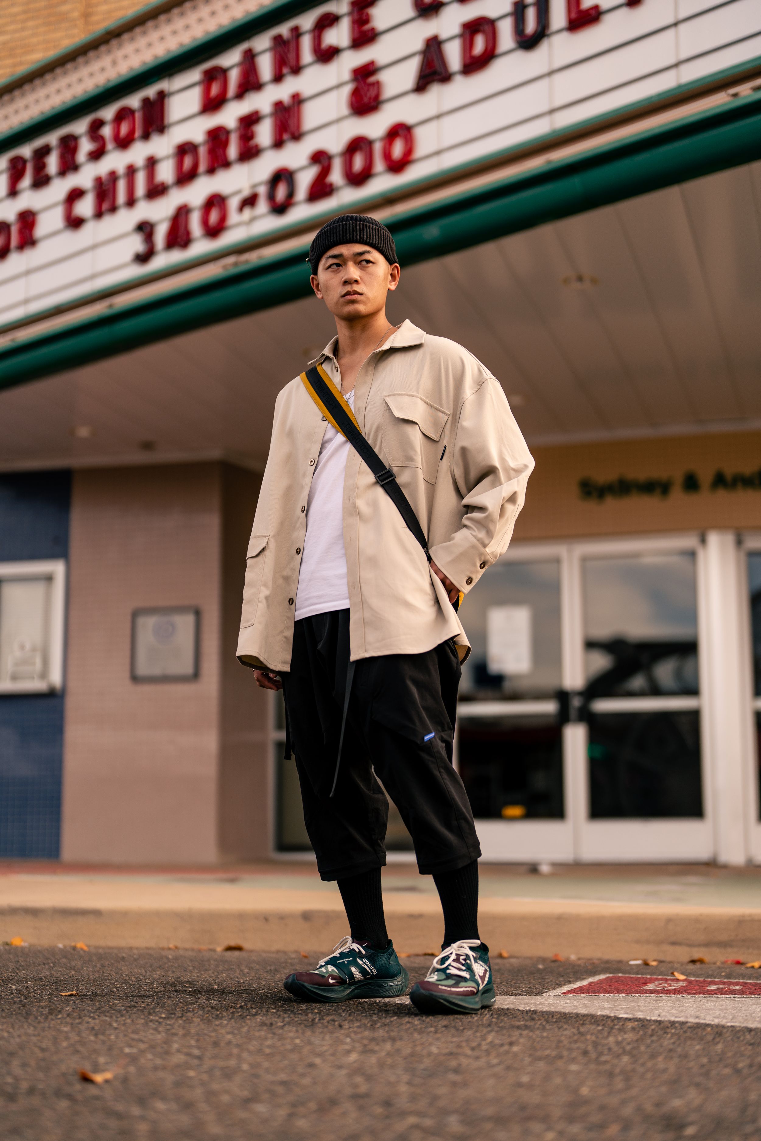 Street style portrait of person in beige jacket and black pants outside dance studio.
