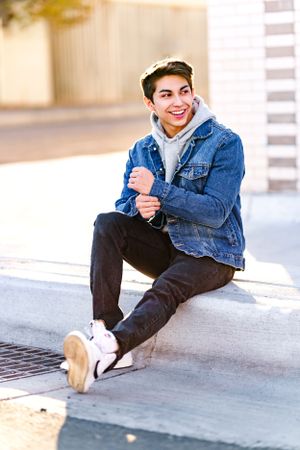 Casual portrait of person in denim jacket and hoodie sitting on concrete steps.
