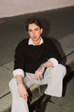 Young model in black sweater and white jeans poses on street corner at night.