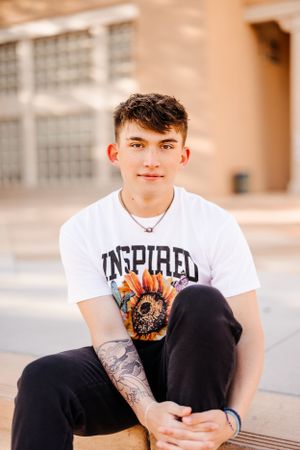 Casual portrait of someone wearing Inspire graphic t-shirt sitting outdoors.