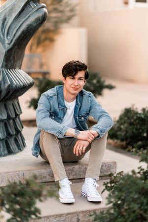 Casual portrait of person in denim jacket sitting on concrete steps outdoors.