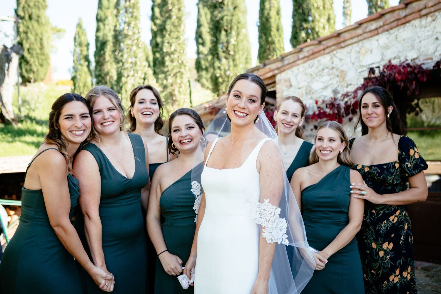 A bride stands in front of her bridesmaids in green dresses smiling.