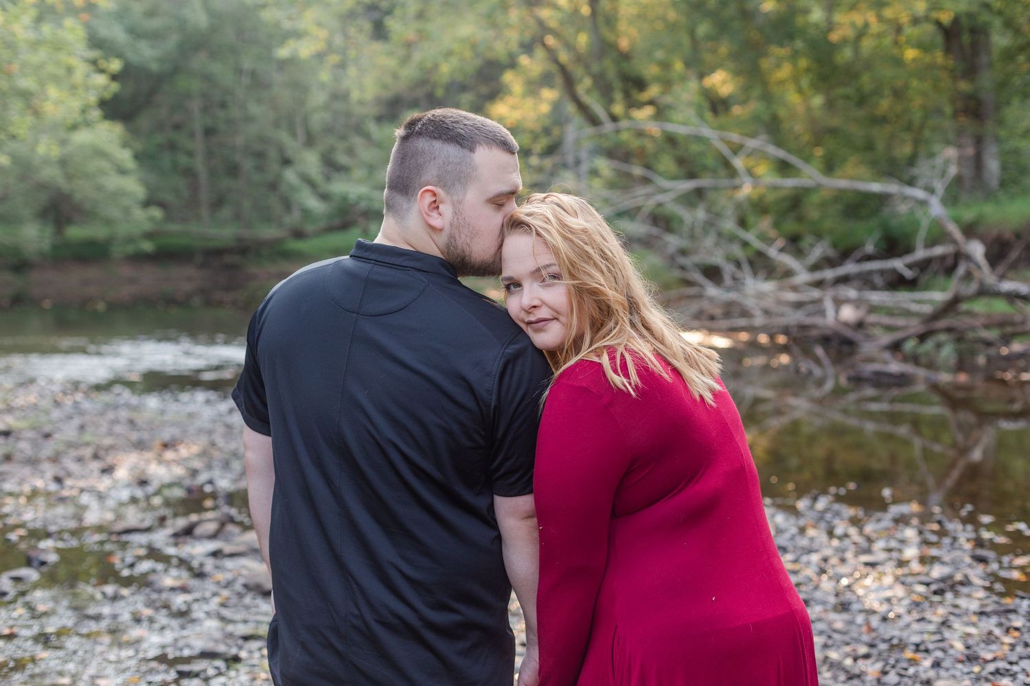 Romantic engagement photo session in a natural outdoor setting with a creek and fallen trees in the background.