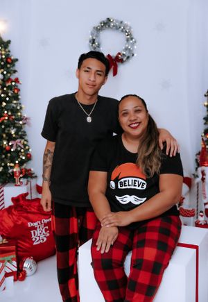 Holiday portrait with Christmas trees and a 'Believe' themed outfit against a festive backdrop.