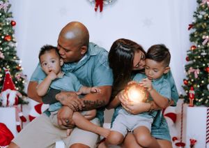 A cozy family moment during Christmas with glowing lights and decorated trees in the background.