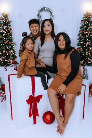 Family in brown and black outfits pose for Christmas photos with decorated trees and red bows.