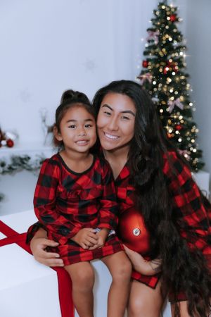 Cozy Christmas photoshoot with matching red buffalo plaid outfits near decorated tree.