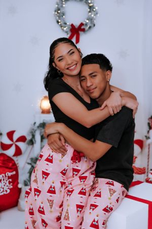 Couple in matching Christmas pajamas posing in front of decorated holiday scene.