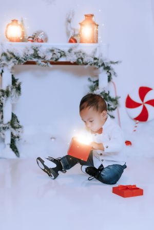 Baby explores Christmas decorations in white winter wonderland setting with red accents.