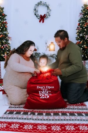Family gathers around a red Christmas bag marked 'Dec 25' with decorative holiday backdrop.