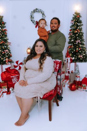 Family poses together on a red and white holiday set with Christmas trees and decorations.