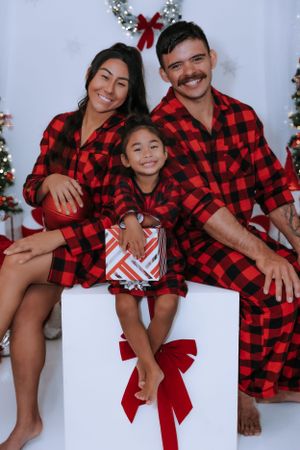 Family wearing matching red buffalo plaid outfits posing for Christmas photos.