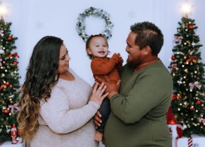 Family shares tender moments during Christmas photo shoot with decorated trees.