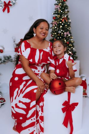 Two people in matching red and white holiday dresses pose playfully against Christmas decorations.