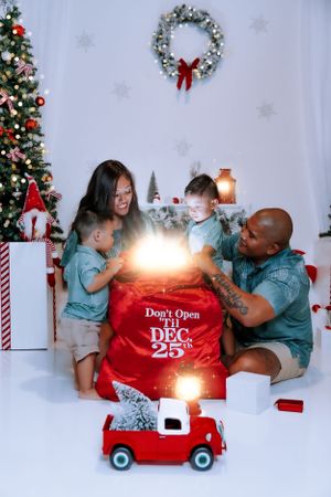 Family gathered around a glowing red Christmas gift box with a vintage toy truck in the foreground.