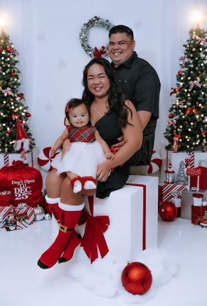 A festive family Christmas portrait with decorated trees, red and white decor, and wrapped presents.