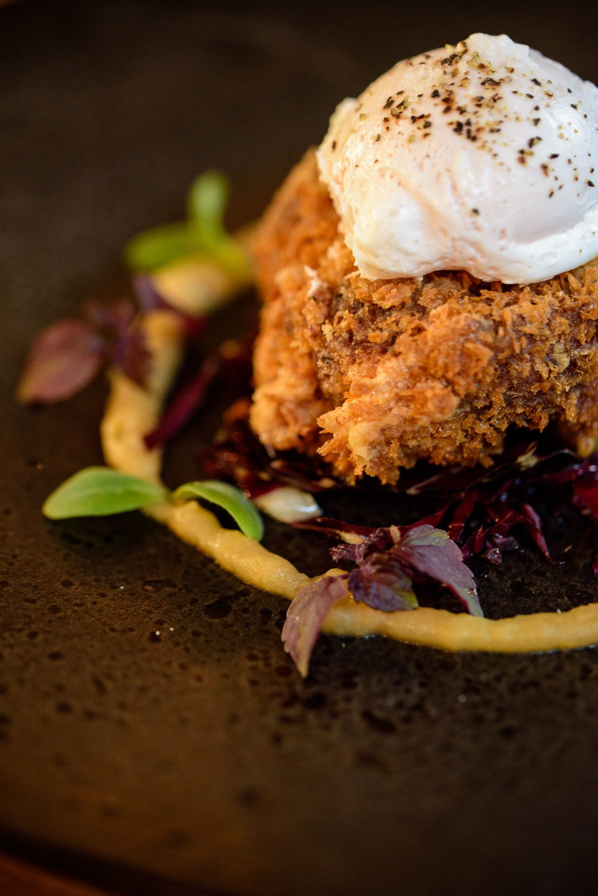 Gourmet dish featuring a poached egg over crispy breading with microgreens.