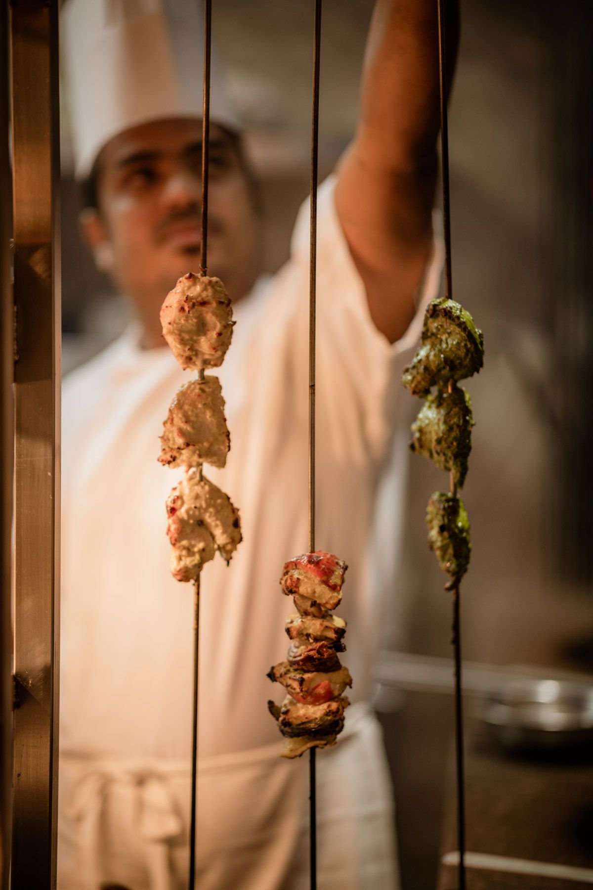 Chef preparing skewered meat and vegetables in a professional kitchen.