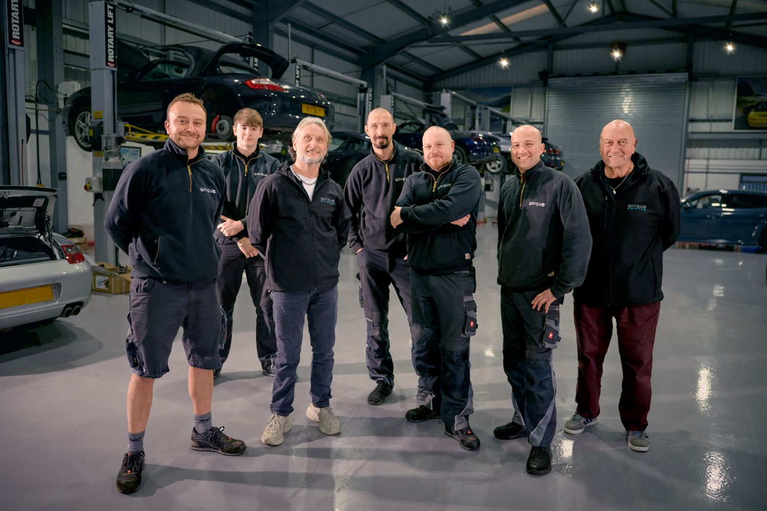 Group photo in industrial warehouse setting with equipment in background.