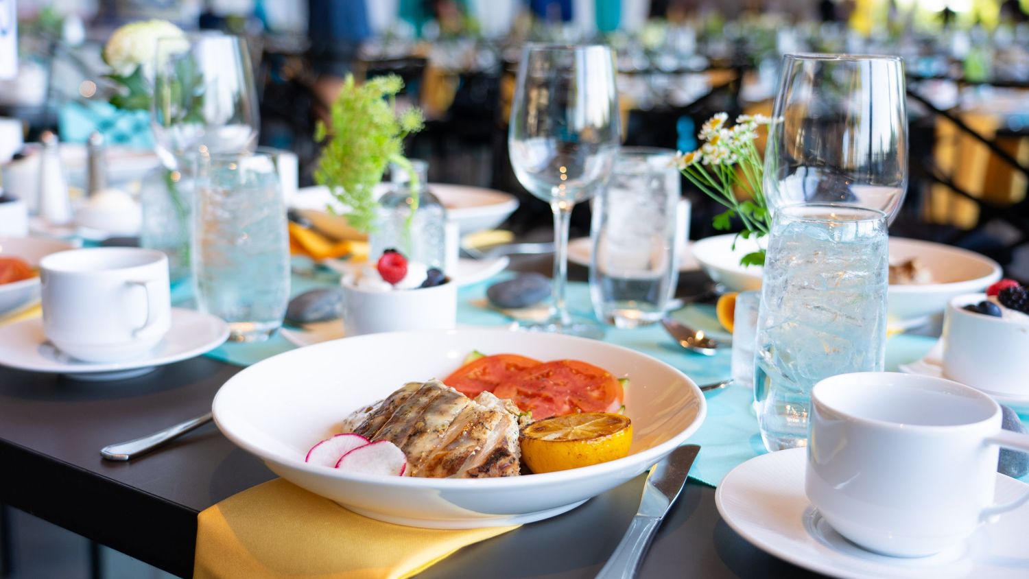 Place setting at elegant restaurant with plated food, wine glasses and table decor.