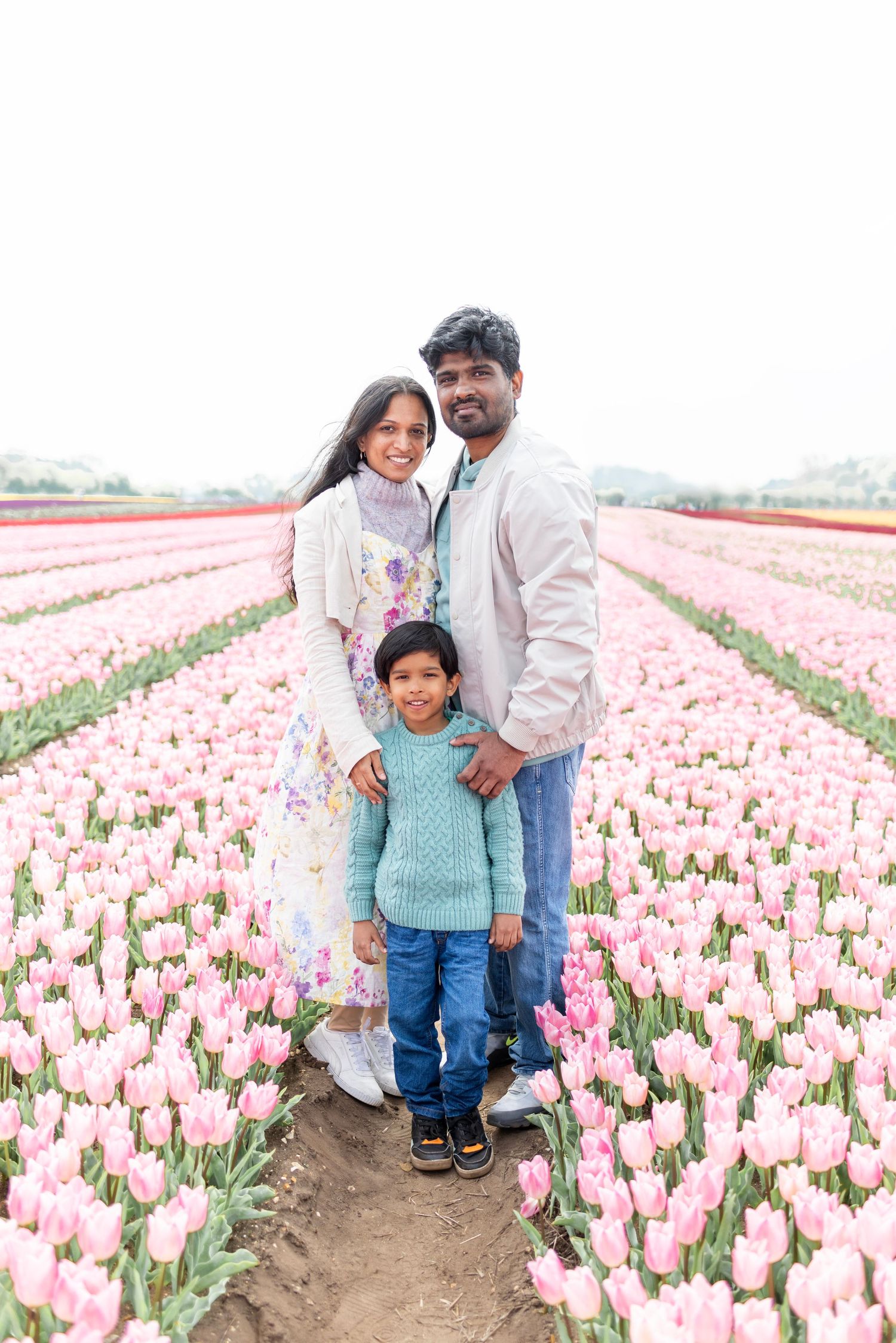 Family of three standing together in a vibrant pink tulip field.