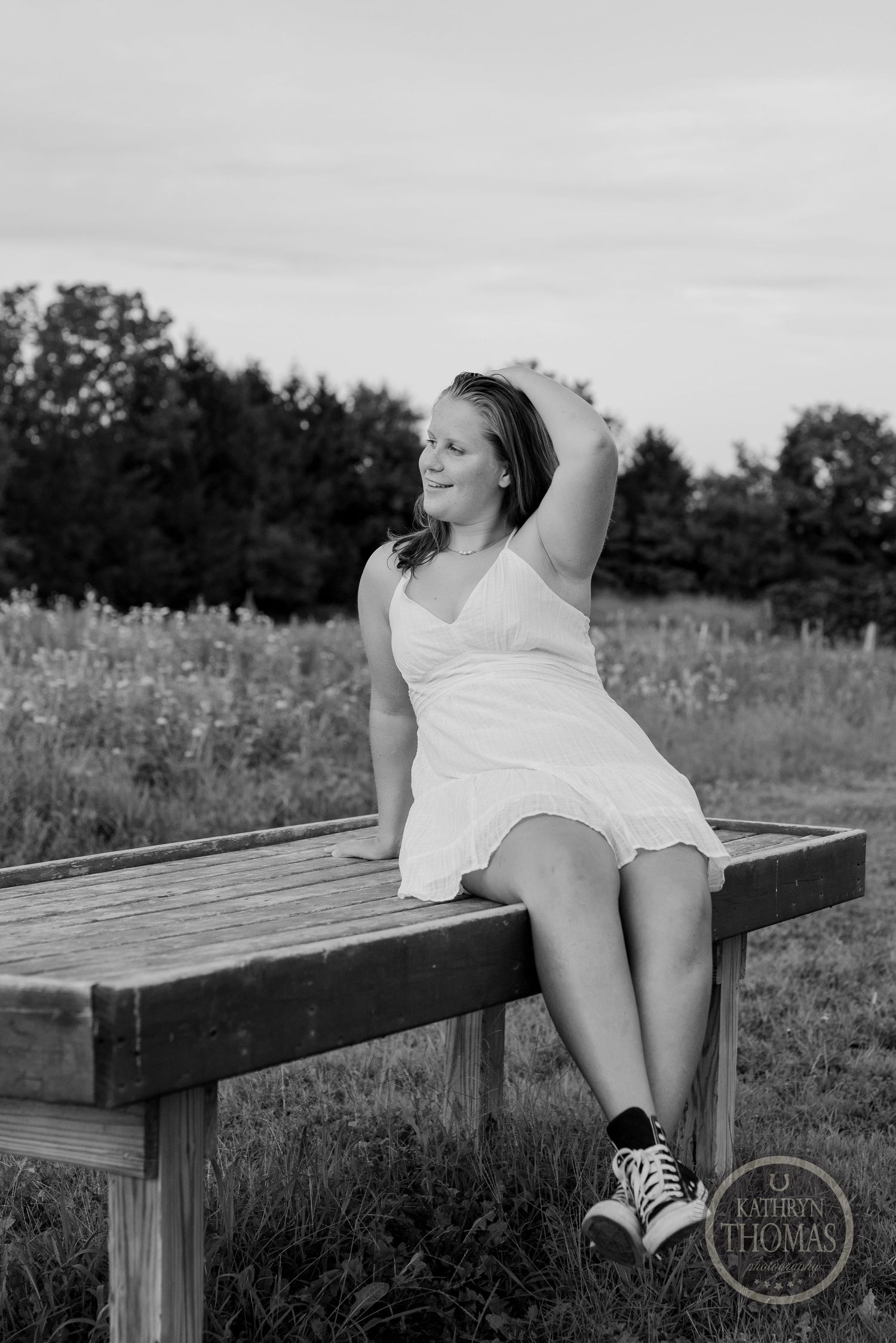 A black and white artistic portrait on a wooden bench in a meadow setting.