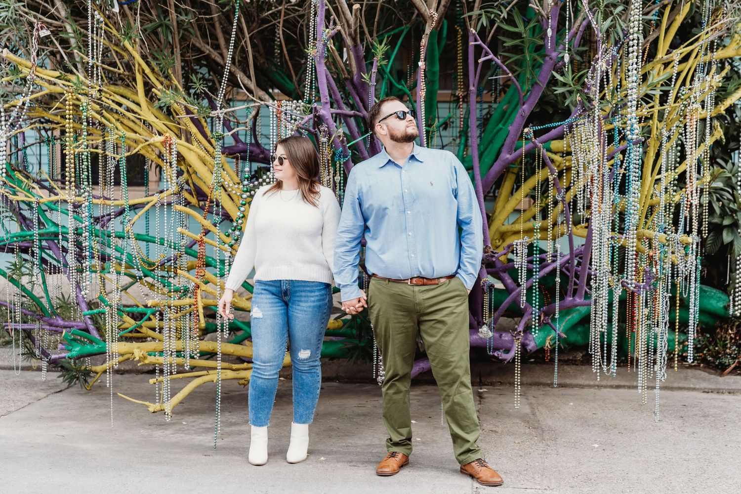 A couple stands together in the middle of a New Orleans area home, with a Mardi Gras tree behind them.