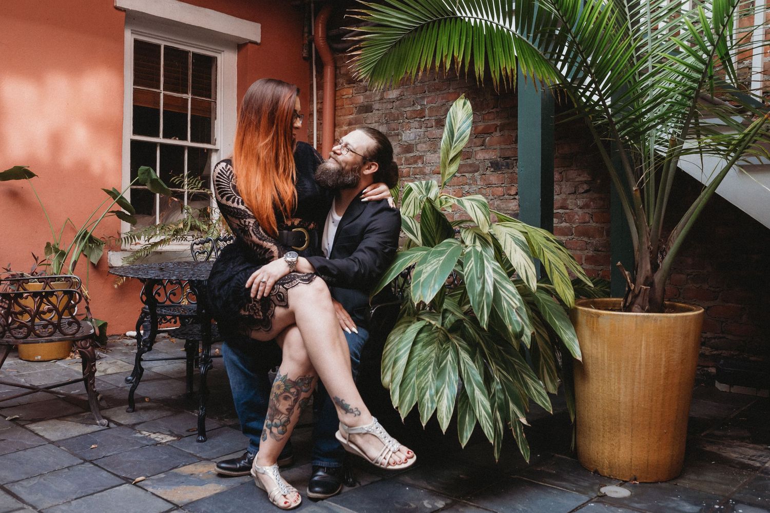 A woman sits on her husbands lap in a French Quarter courtyard.