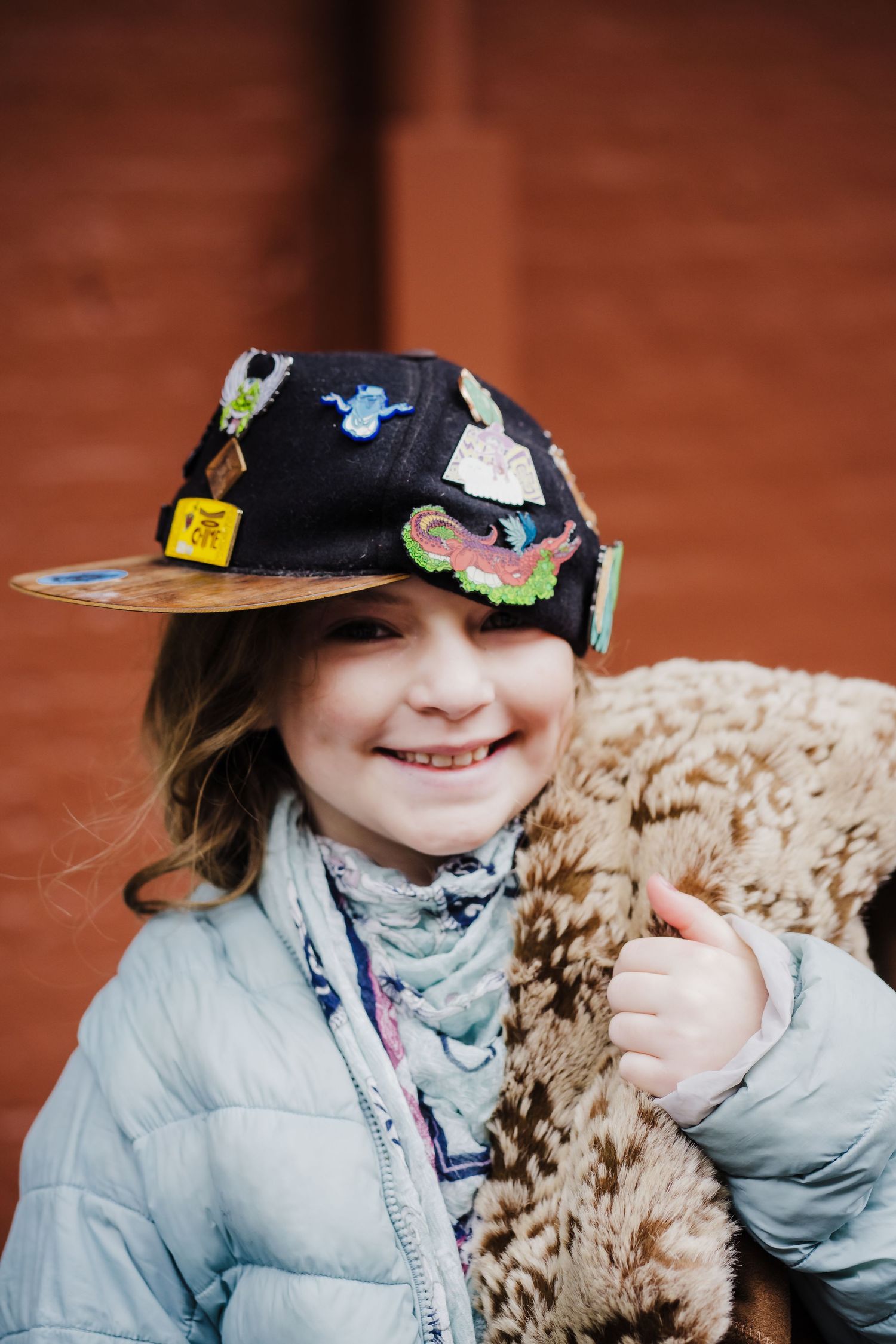 Young girl wears her dad's baseball hat and laughs while carrying a purse.