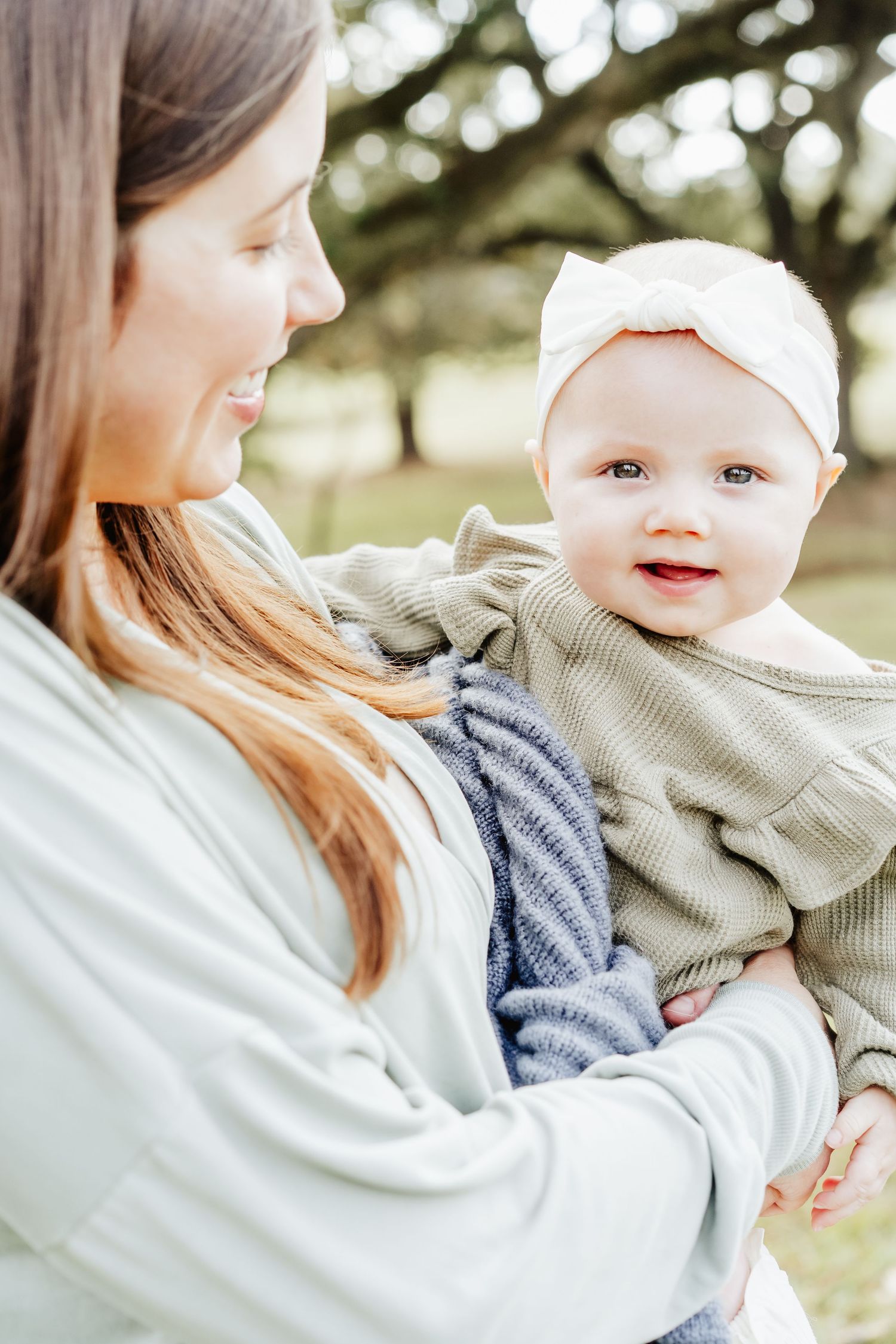 A baby smiles as her mother holds her on her hip.
