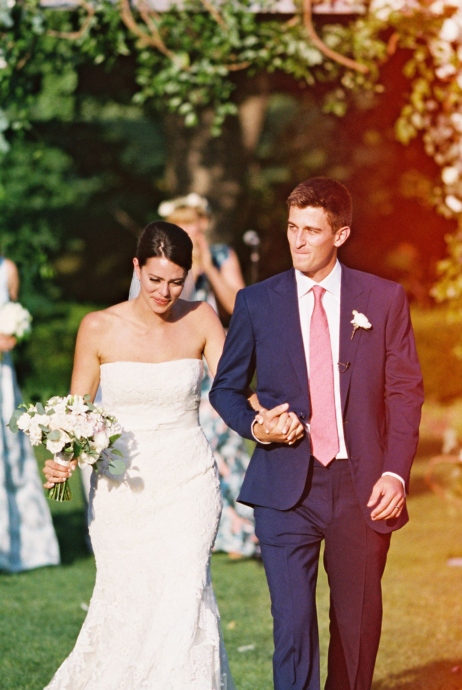 A bride and groom walk hand in hand down the aisle after their outdoor summer wedding ceremony.
