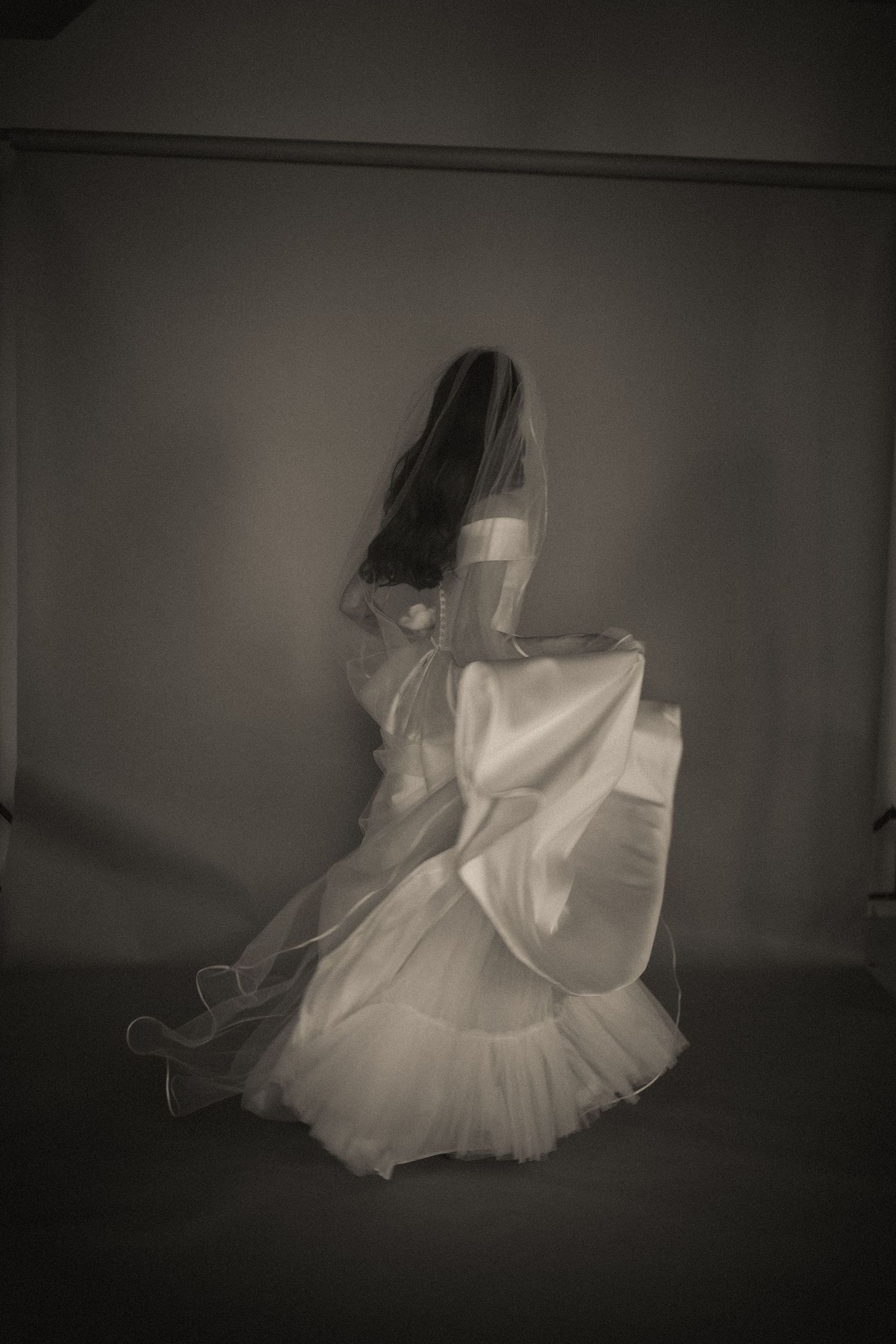 A bride in a full tulle wedding gown and veil twirling in a dramatic black and white photo.