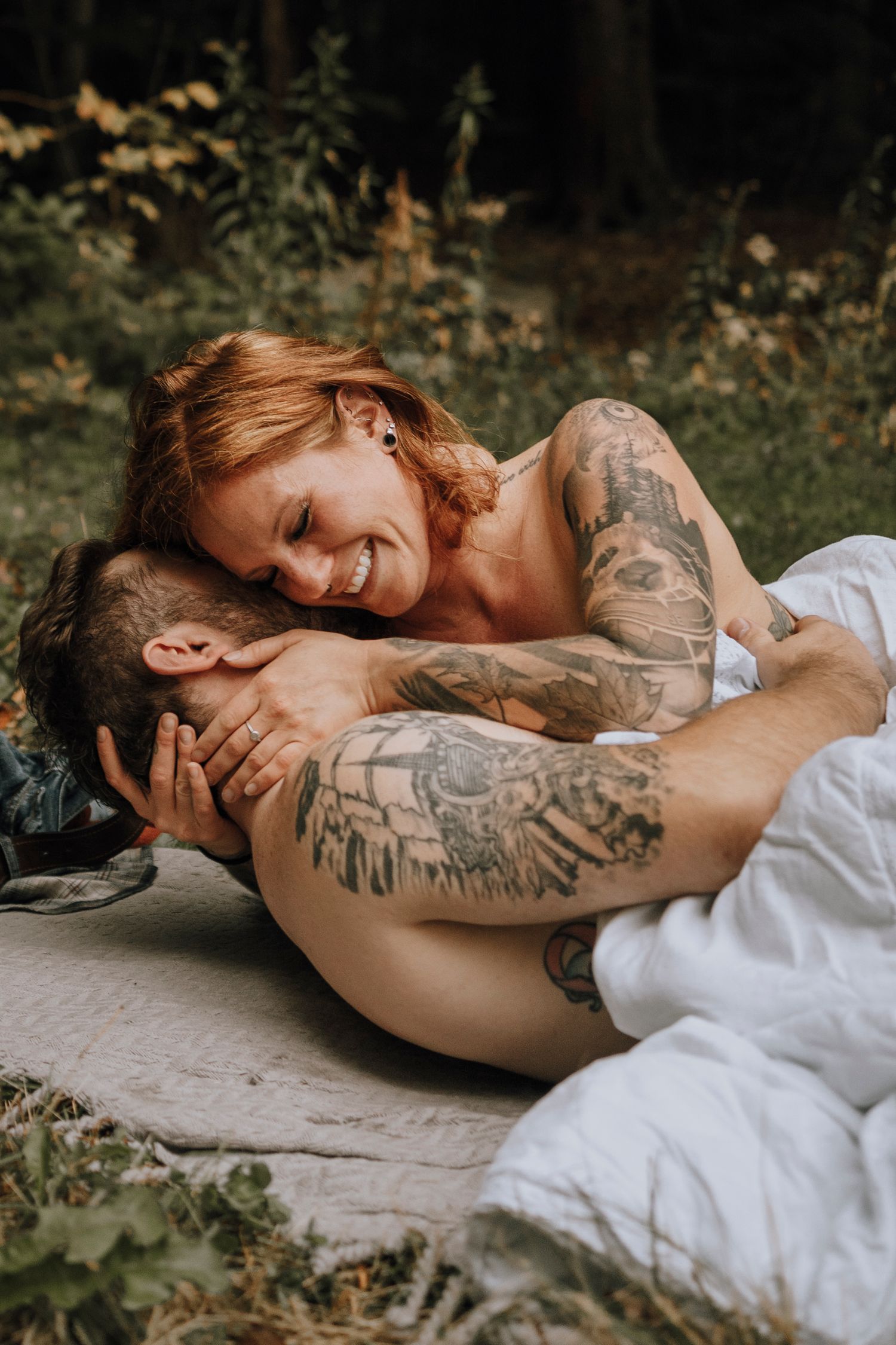 Romantic outdoor portrait of tattooed couple laying on blanket in garden setting.