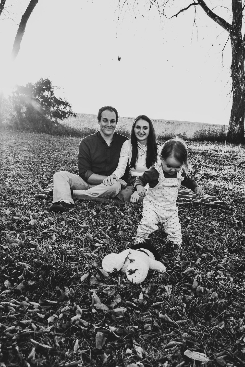 Family relaxes together on fallen leaves during an outdoor black and white photoshoot.