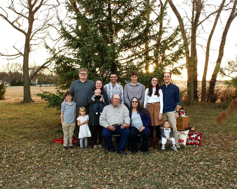 Large family group poses together on fallen autumn leaves at sunset.