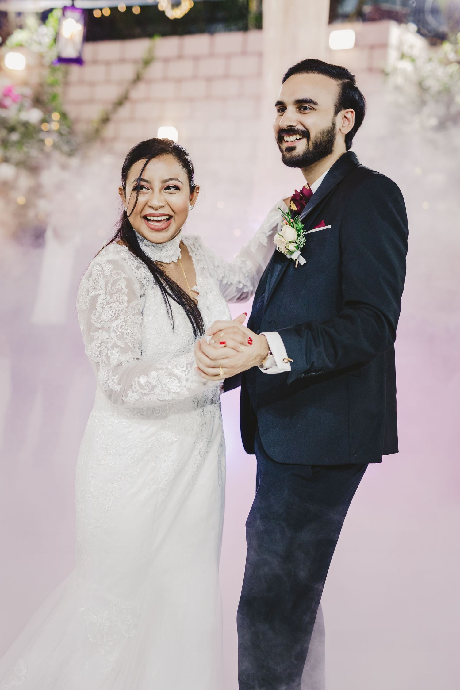 Couple sharing their first dance in an elegantly decorated reception space with pink lighting.
