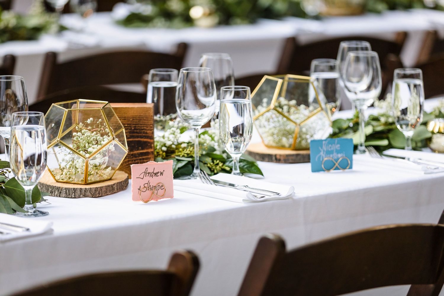 Wedding table decor featuring geometric terrariums, wooden chargers, and delicate greenery arrangements.