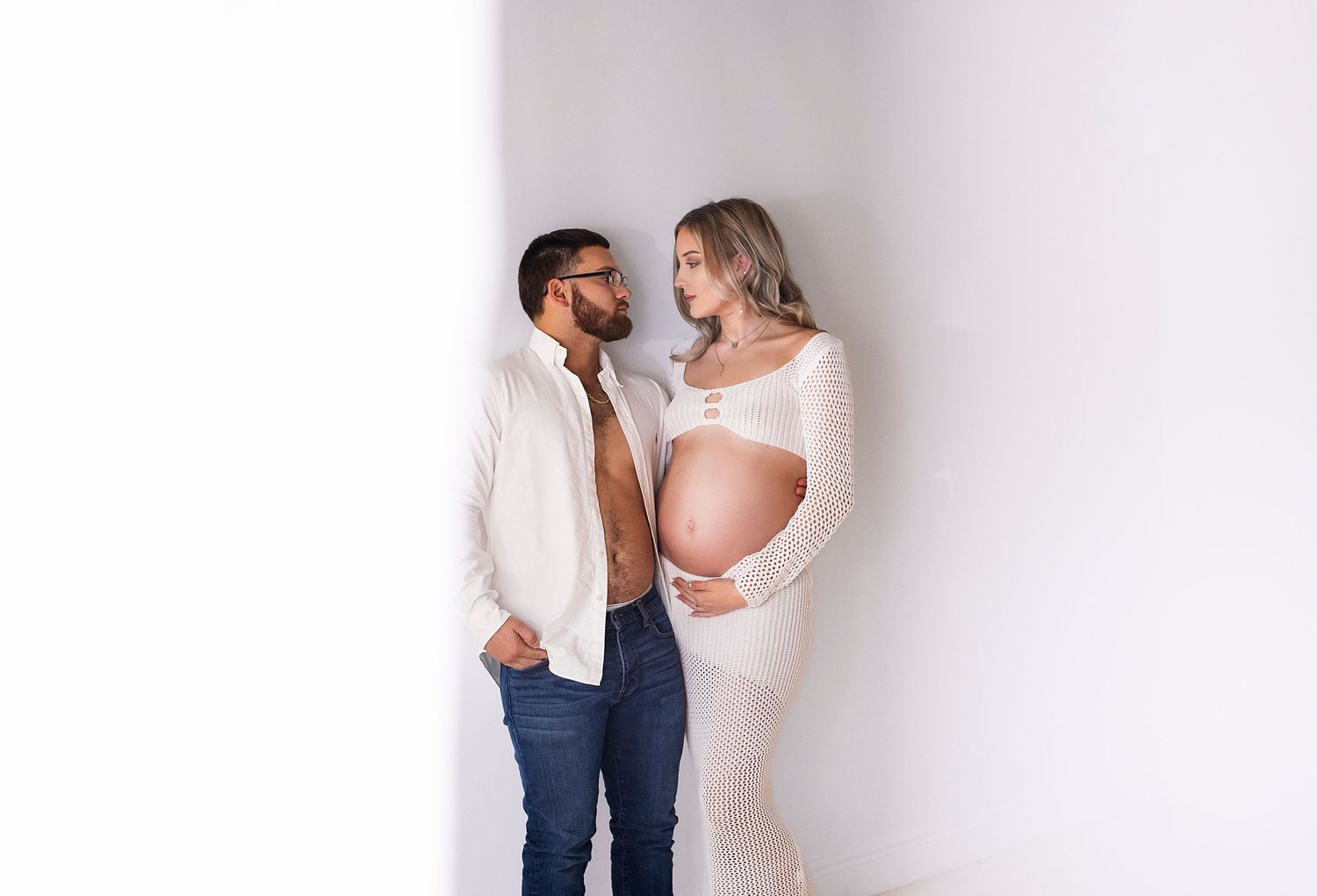 Couple in a maternity shoot with the mother in a knit dress, showcasing her baby bump, and the father looking on adoring
