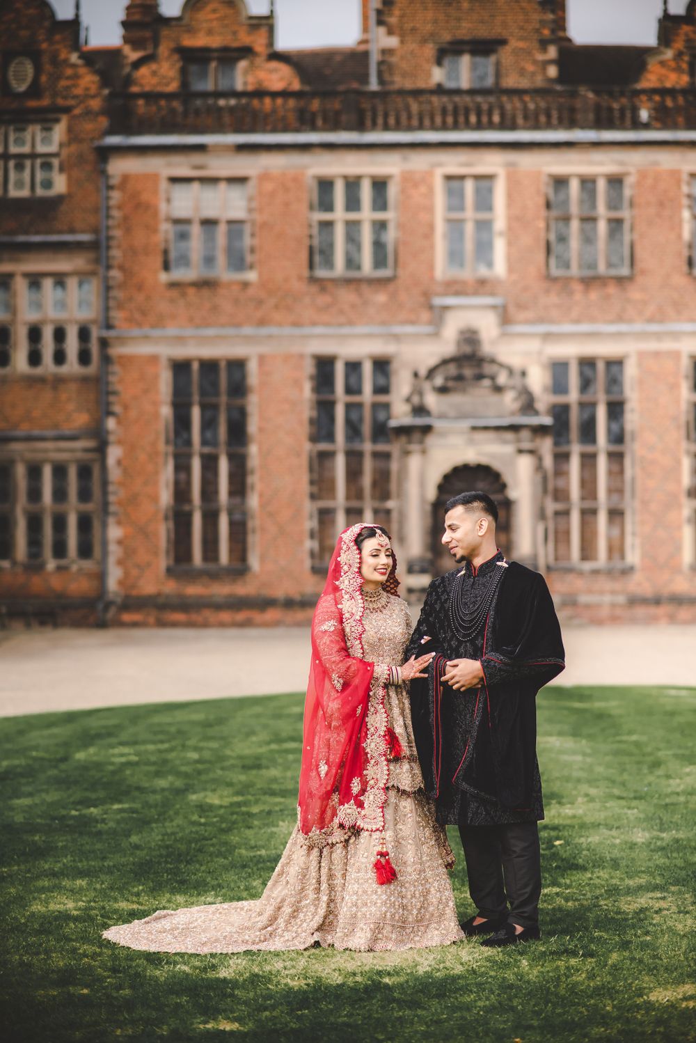 A wedding couple shares a joyful moment on the lawn of a grand manor house.