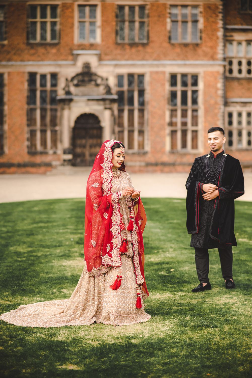 A wedding couple poses against the backdrop of a stately brick manor house.