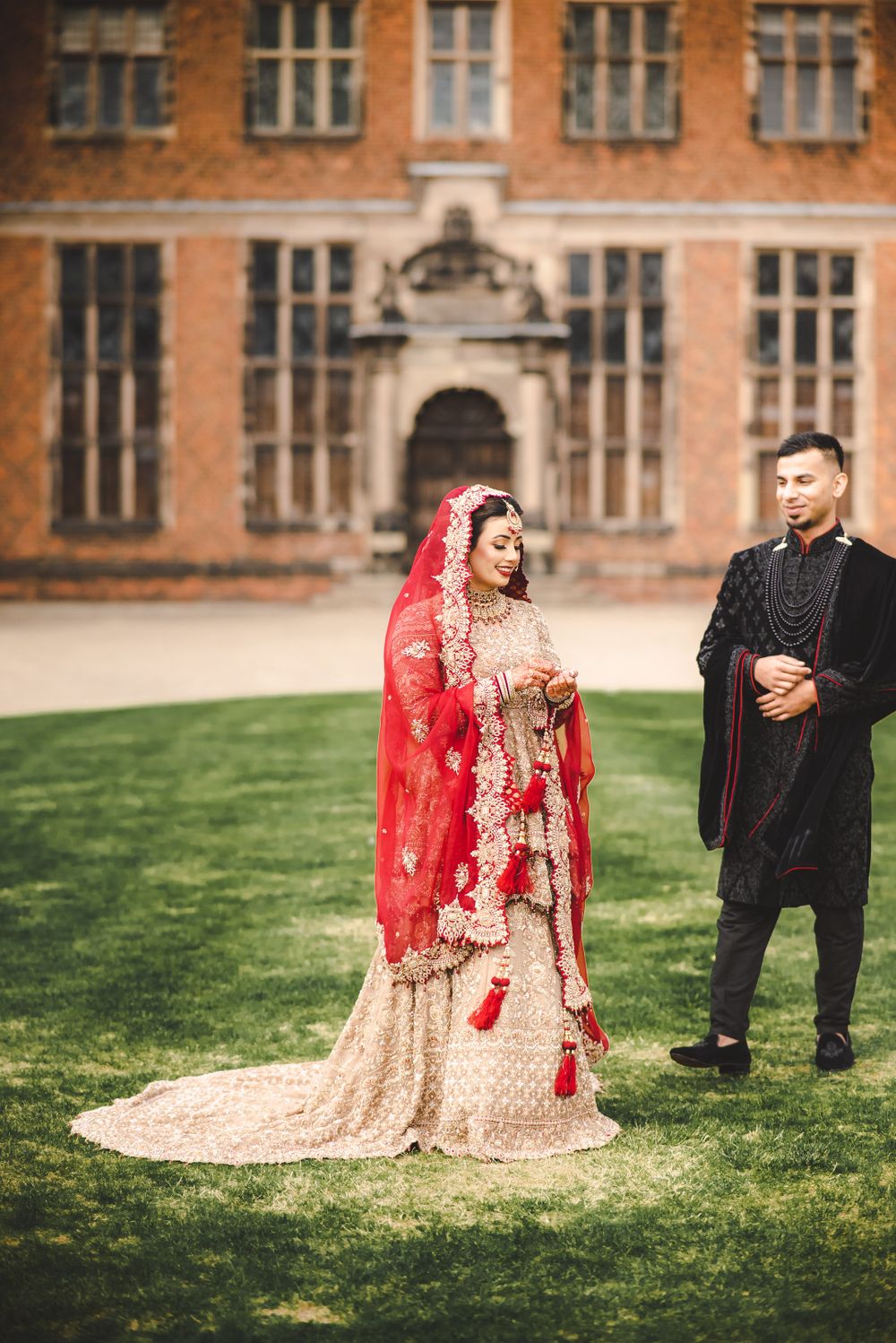 A couple in traditional South Asian wedding attire photographed against historic manor backdrop.
