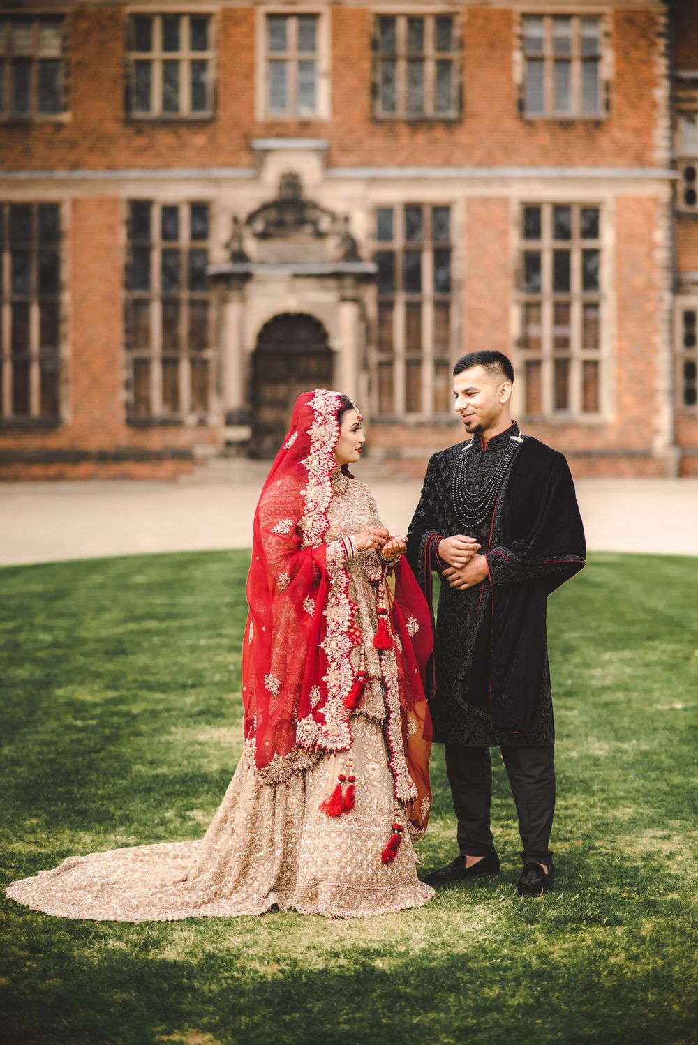 A wedding couple in traditional South Asian attire stands before a grand historic facade.