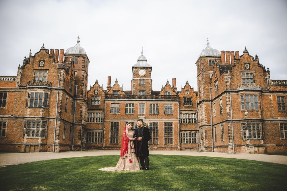 Couple standing on lawn before grand historic British architecture during wedding photoshoot.