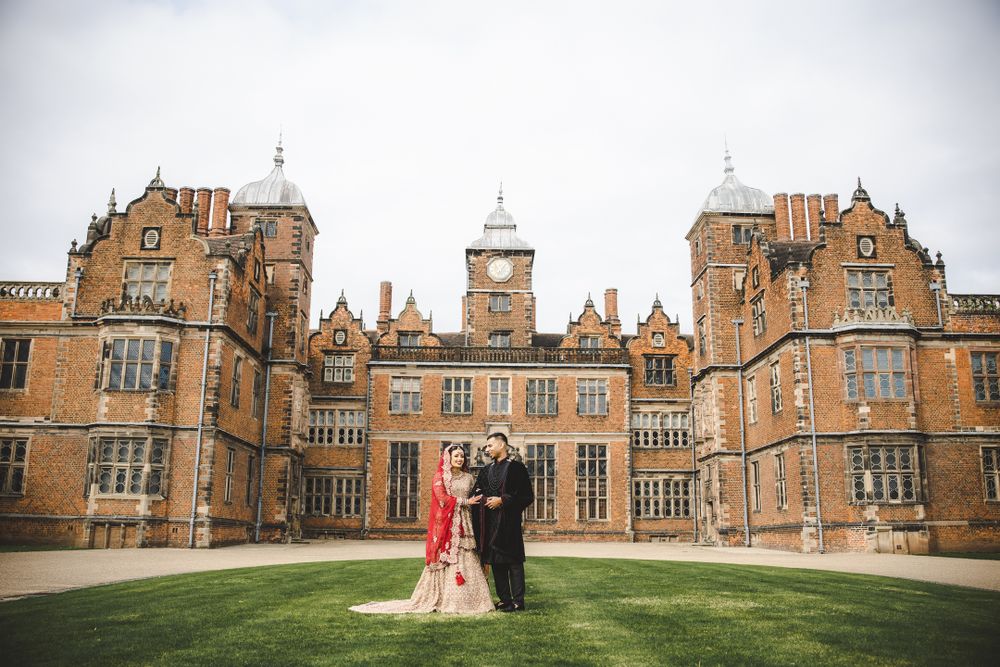 Wedding portrait with couple on green lawn in front of ornate Gothic revival architecture.