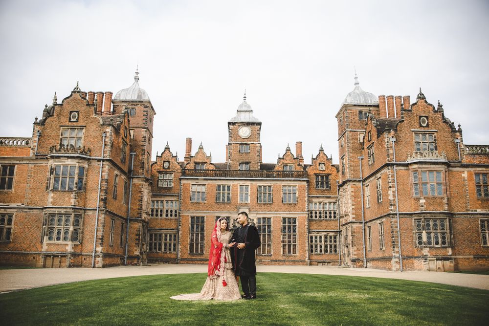 Elegant wedding photo featuring couple against backdrop of magnificent Tudor-style mansion.